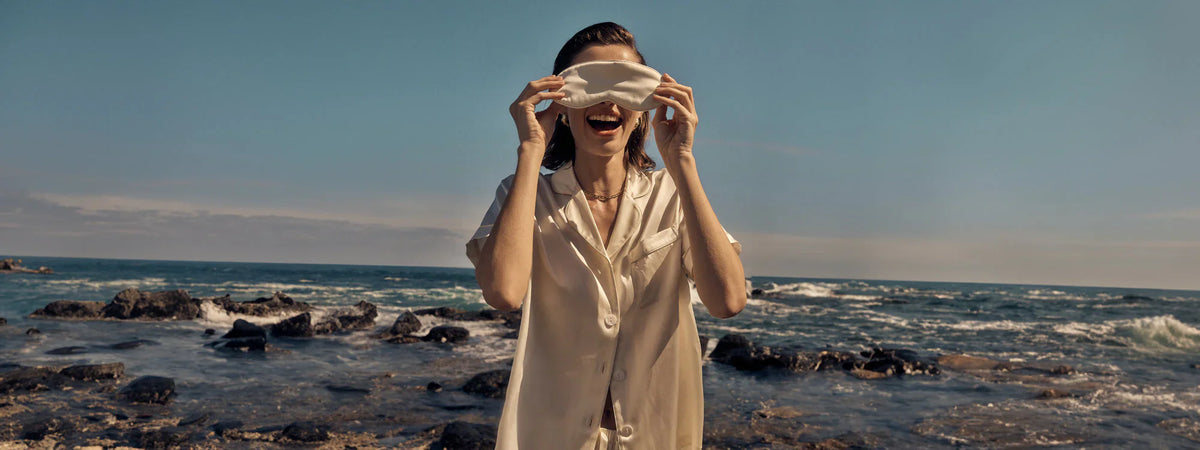 Woman in silky Gingerlilly Sleepwear and eye mask by the ocean on a rocky shore
