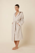 Woman wearing a striped adriana terry towel robe in biscuit colour standing against a plain background from a side on view