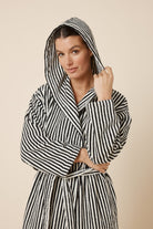 Woman wearing a striped adriana terry towel robe in black colour upper body view with her hold the hood which is on her head
