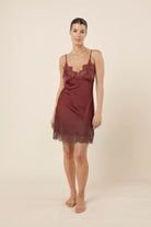 Woman wearing Azalia Silky Satin Short Chemise Burgundy standing facing forward, showing the silky satin slip dress with thin straps, lace neckline and soft drape.