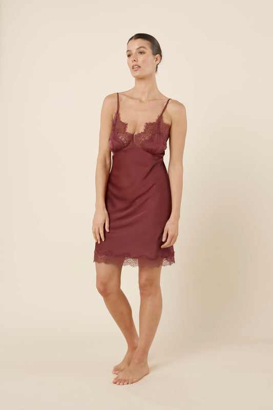 Woman wearing Azalia Silky Satin Short Chemise Burgundy walking slightly forward, showing the smooth satin slip shape, lace neckline and softly moving hem.
