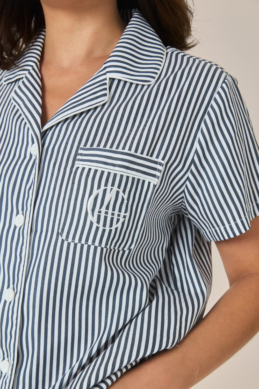 Close-up of the collar and embroidered logo pocket on a navy and white striped pyjama shirt.
