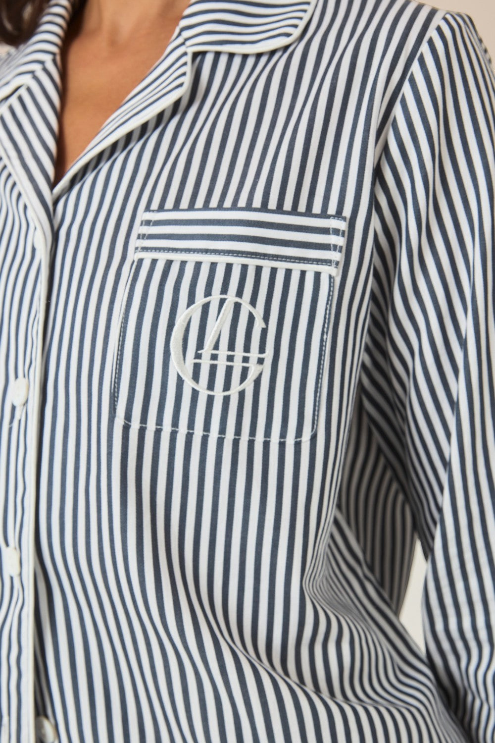 Close-up of the collar and embroidered logo pocket on a navy and white striped pajama shirt.