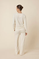 Woman wearing a ellie lightweight velour cable knit set ivory long-sleeve top and pants on a beige background back view