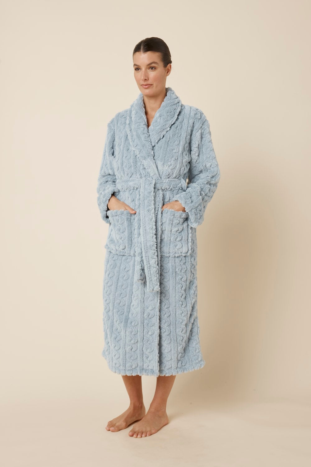 Woman wearing a textured blue Gabriella Plush Long Robe with her hands in both pockets and waist tie done up