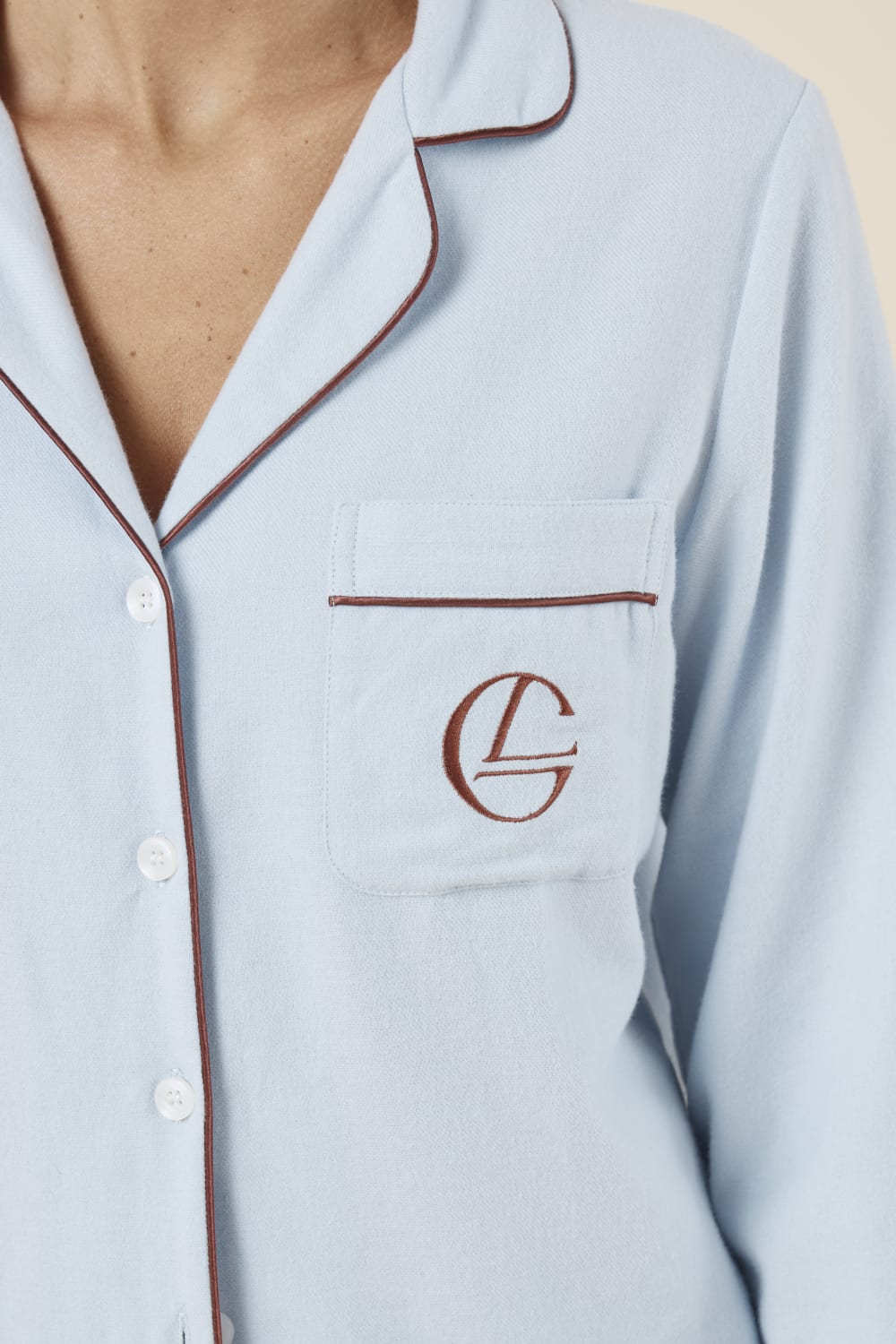 Woman wearing light blue isabella brushed cotton pyjama PJ set with a small red logo on pocket with red pip detailing and white buttons showing