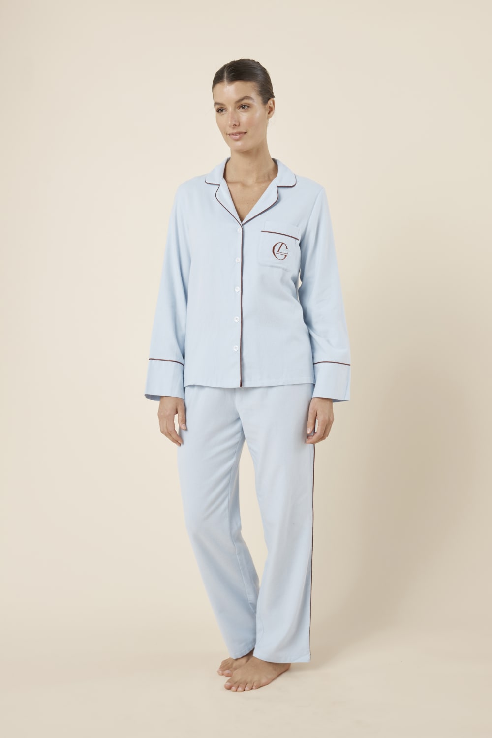 Woman wearing light blue isabella brushed cotton pyjama PJ set with a small red logo on a beige background side on view