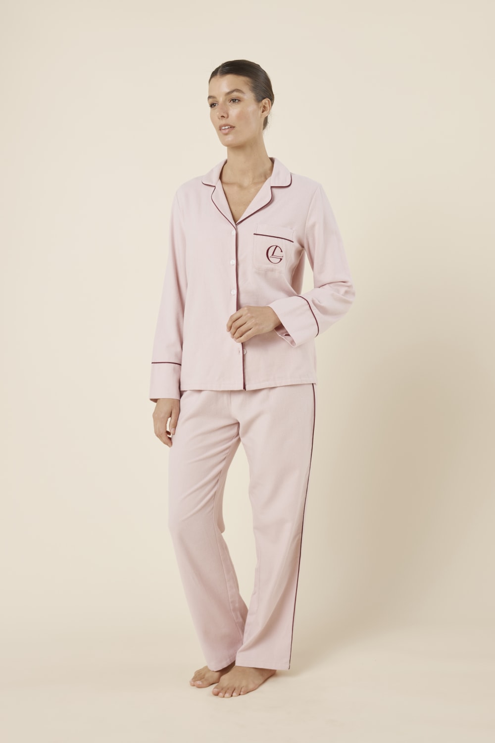 Woman wearing light pink isabella brushed cotton pyjama PJ set with a small red logo on a beige background side on view