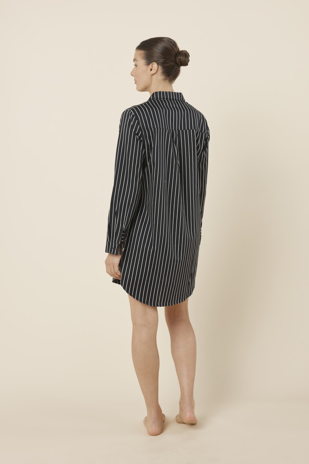 Woman wearing a black and white striped Lolita Stripe Night Shirt dress against a beige background back view