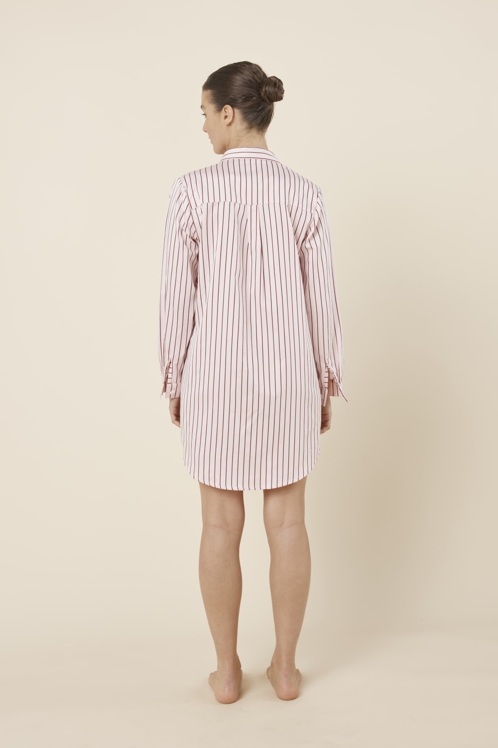Woman wearing a pink striped Lolita Stripe Night Shirt dress against a beige background back view with arms beside her