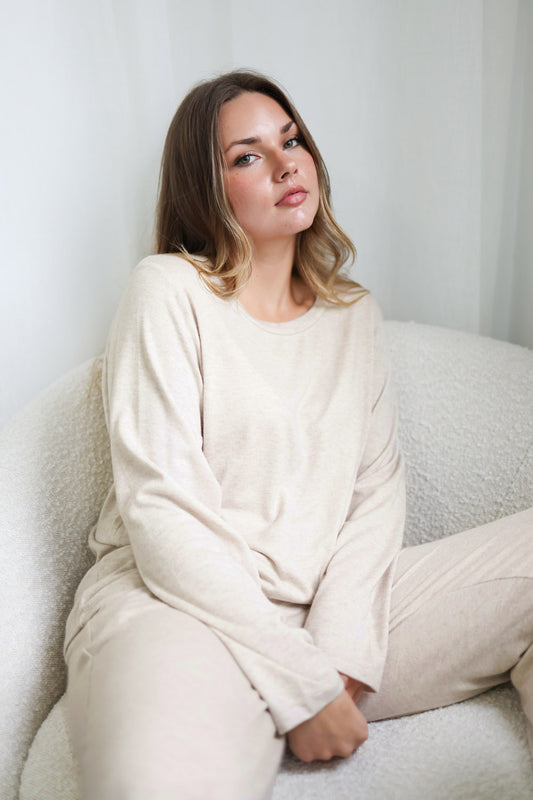 Woman wearing a cream-colored loungewear set sitting on a white couch.