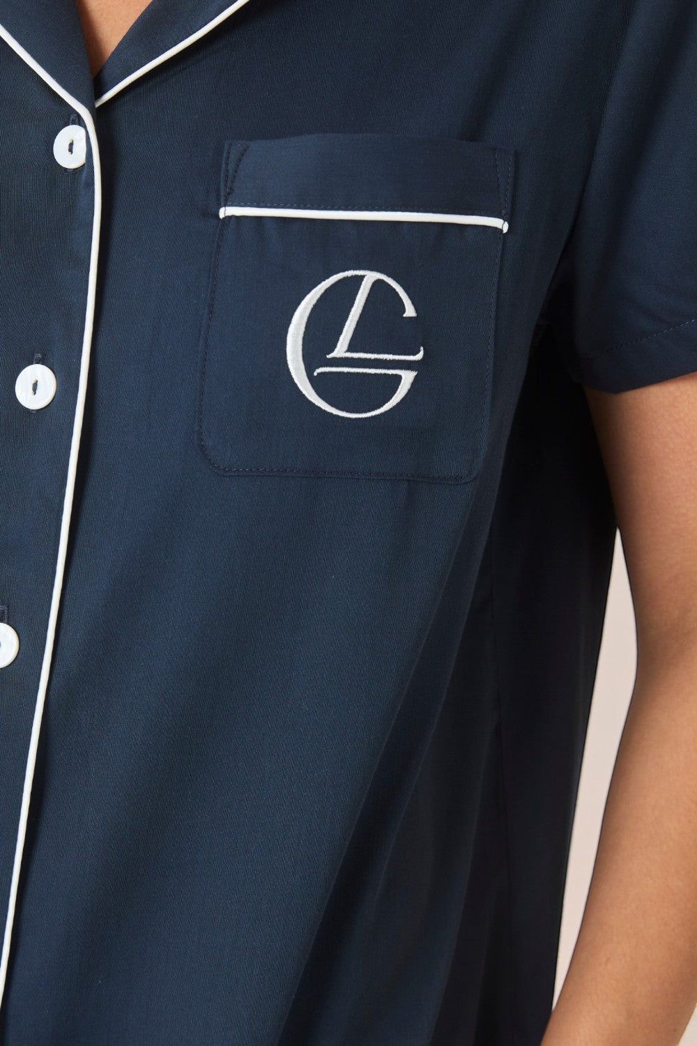 Close-up of the embroidered logo pocket and white contrast piping on a navy pyjama shirt.