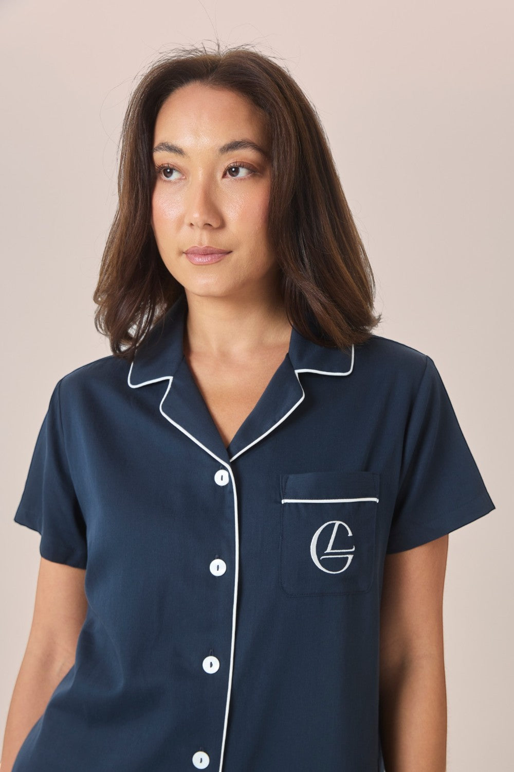 Close-up of a woman wearing a navy pyjama shirt with white contrast piping and an embroidered logo pocket.