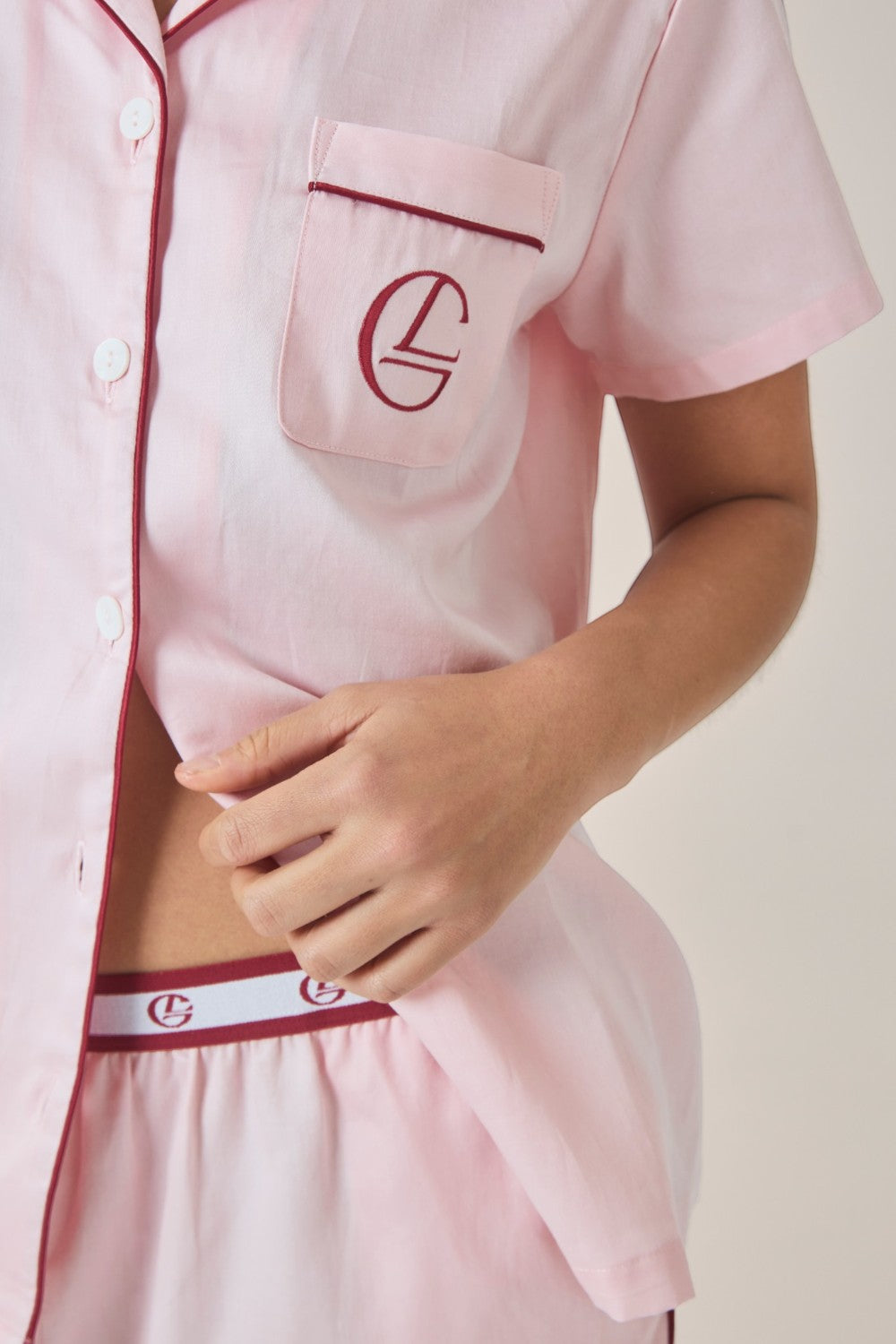 Close-up of a pale pink pyjama shirt and pants, showing the contrast burgundy piping and branded elastic waistband.