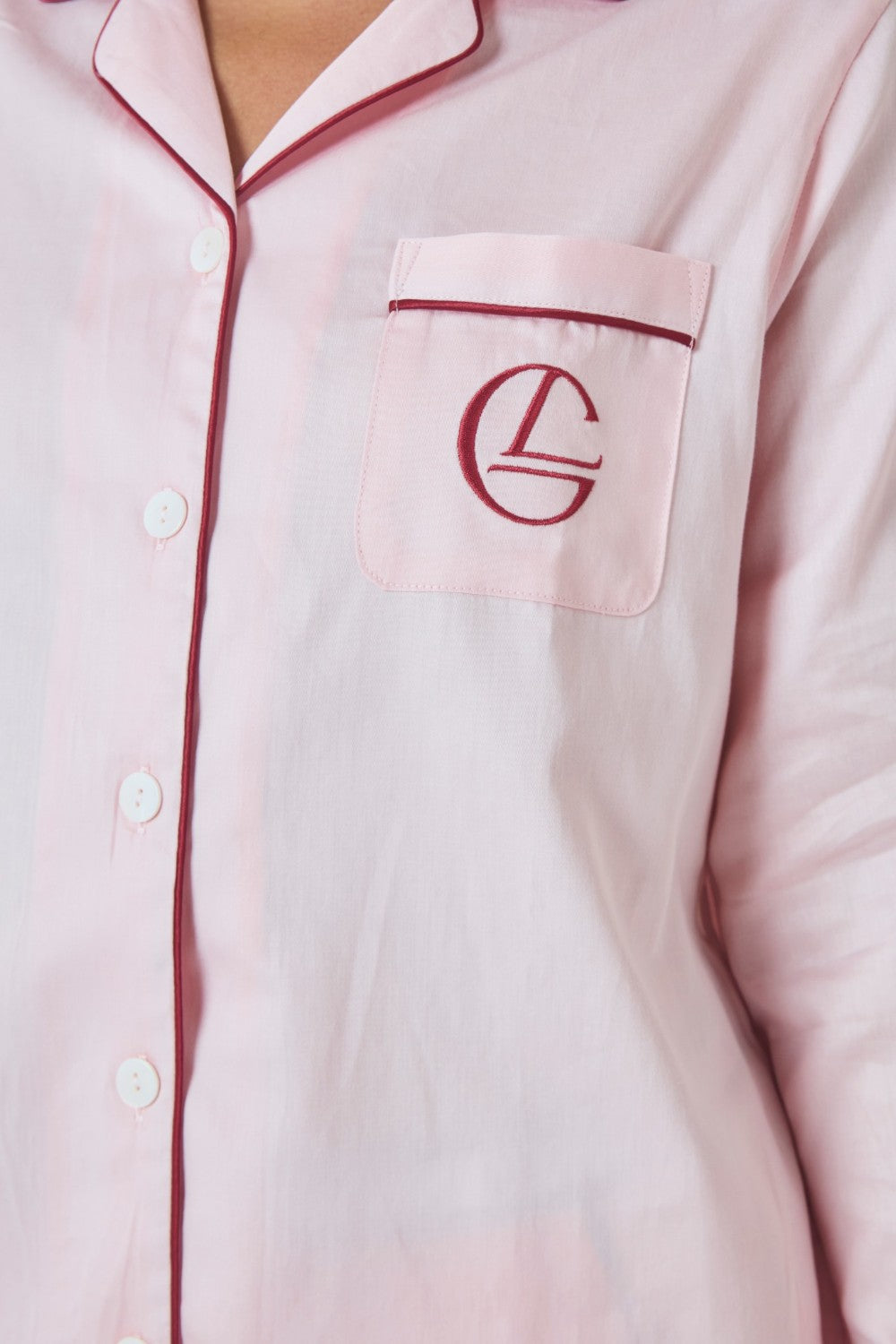 Close-up of the embroidered logo pocket on a pale pink pajama shirt with contrast burgundy piping.