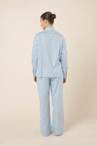 Woman wearing a blue striped willow cotton stripe pyjama PJ set on a beige background and back view