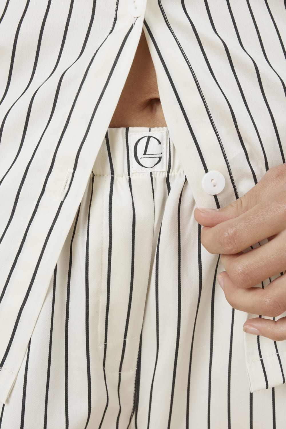 Close up of top of a woman wearing a black and white ivory pin striped willow cotton stripe pyjama PJ set showing the waistline and gingerlilly embroidery with white buttons and pin stripe detail