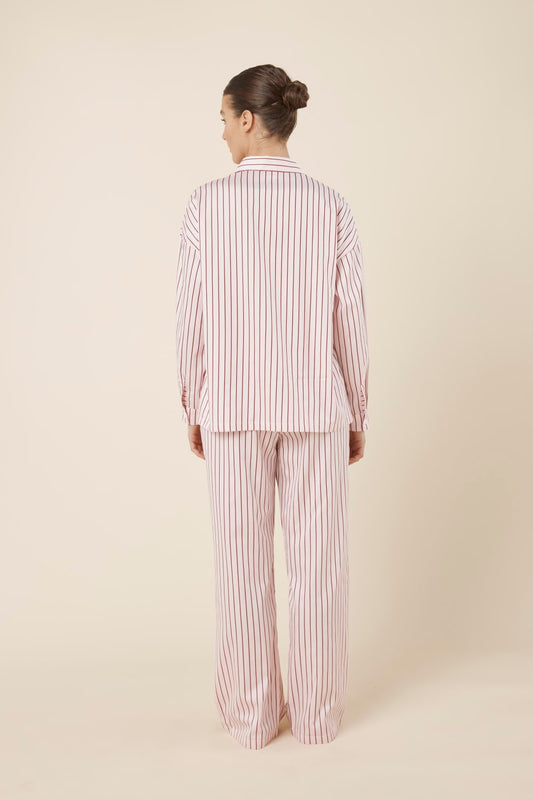 Woman wearing a pink striped willow cotton stripe pyjama PJ set in set on a beige background and back view