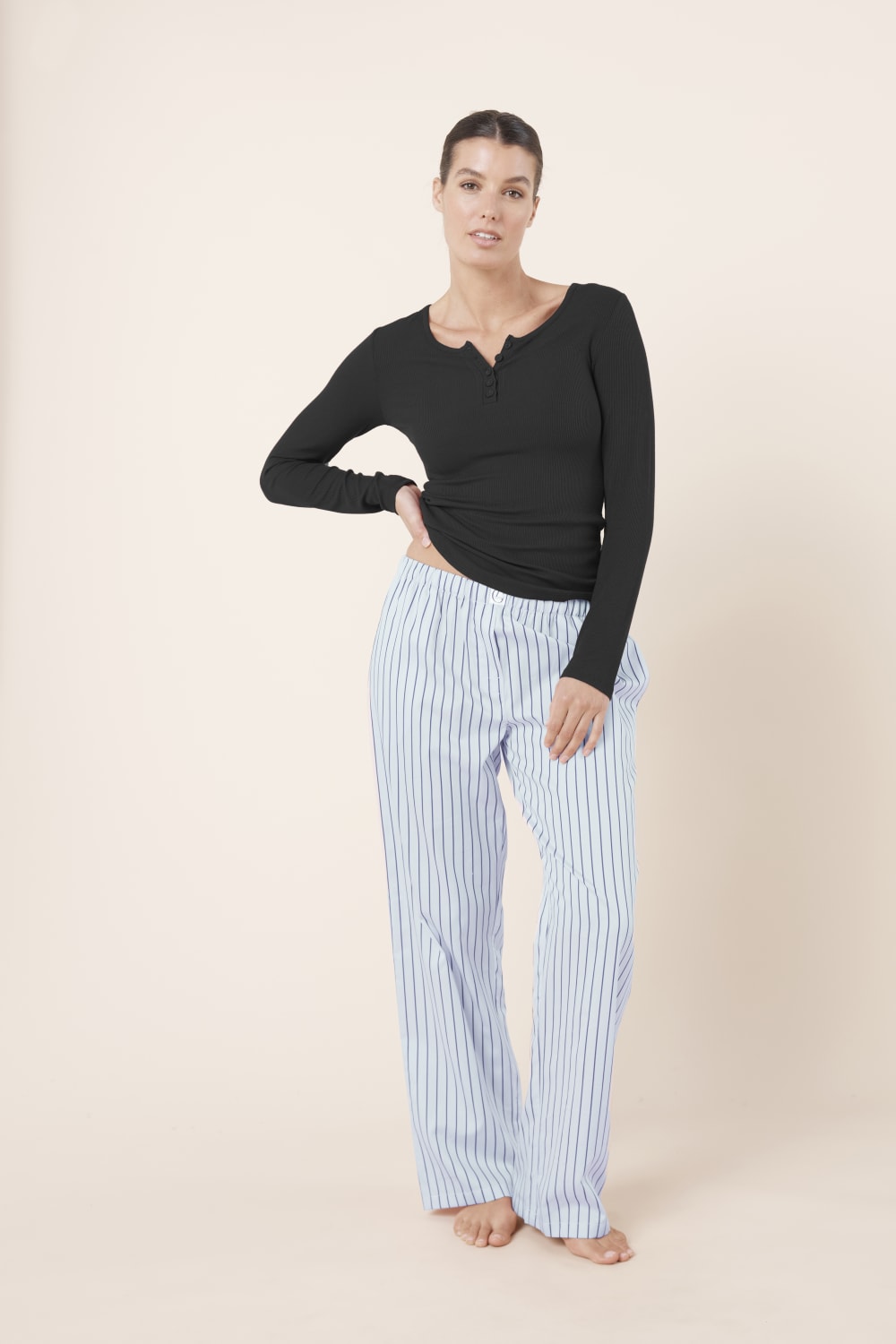 Woman wearing a black long-sleeve top and Willow Cotton Striped Pants in Blue front view on a beige background
