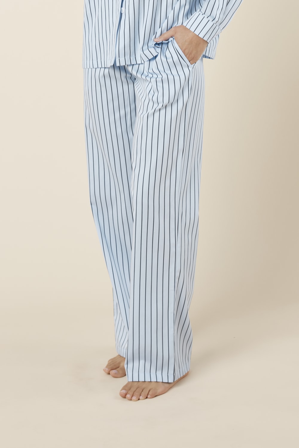 Person wearing willow cotton striped pyjama pants in blue on a beige background side view. 