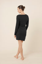 Woman wearing a black bonnie ribbed long sleeve midi henley nightdress against a beige background back view