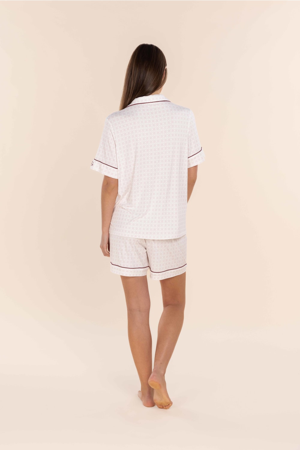 Woman wearing a white pajama set with black piping on a beige background