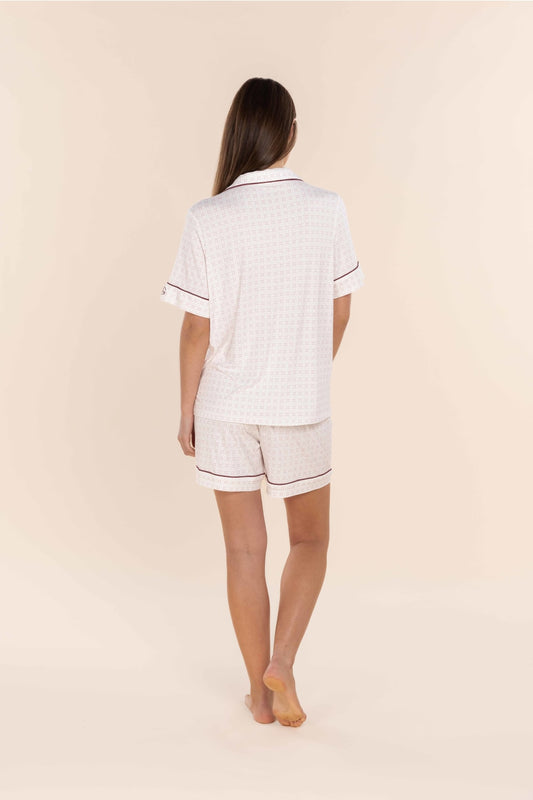 Woman wearing a white pajama set with black piping on a beige background